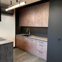 Nowoczesna kuchnia z frontami w odcieniach brązu i szarości. Złota bateria i industrialna lampa nad blatem dodają elegancji. Minimalistyczny design.