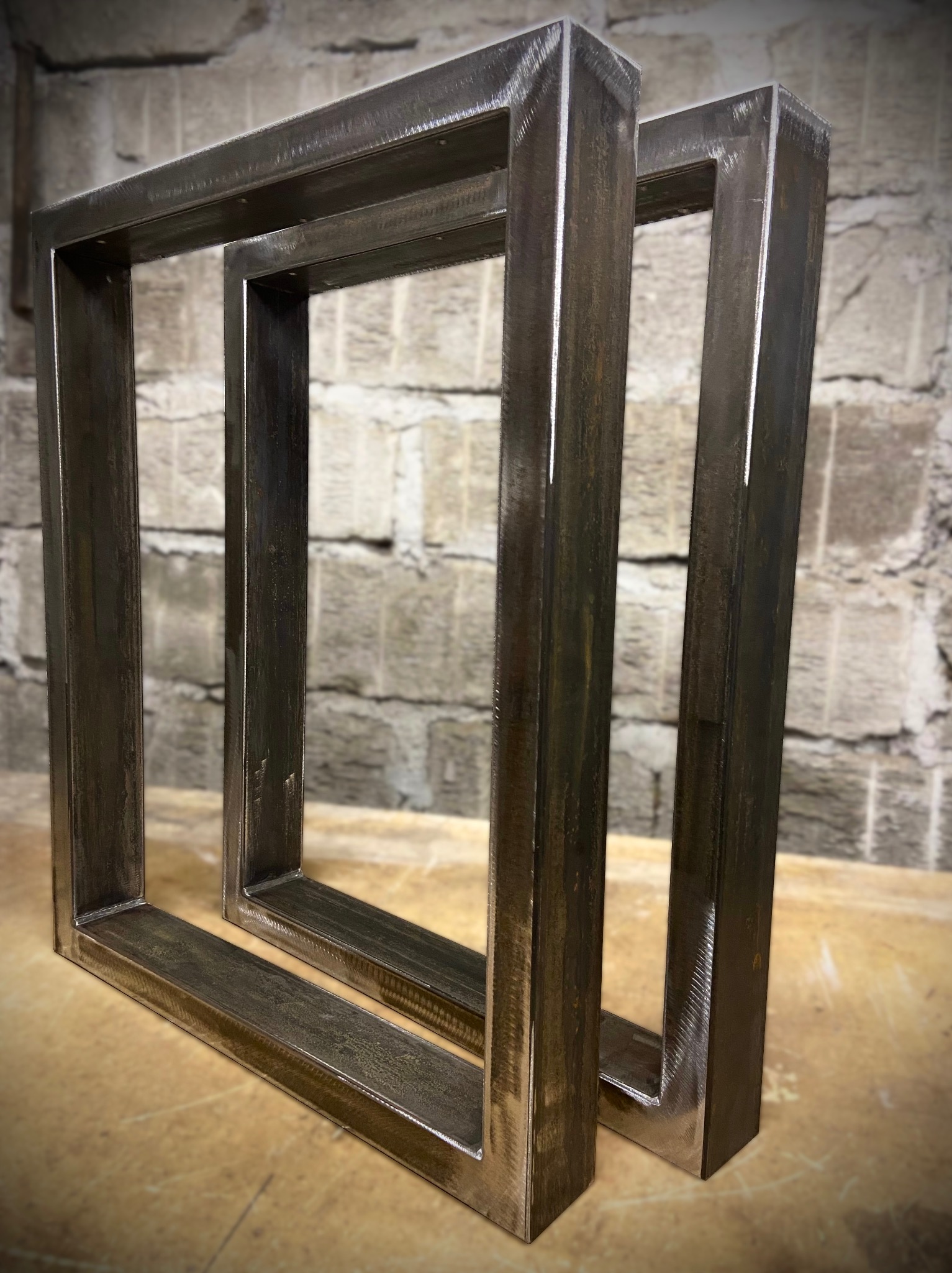 Dwie metalowe ramy spawane z profili kwadratowych, ustawione pionowo na stole warsztatowym, widoczne ślady po spawaniu i szlifowaniu, surowy wygląd.