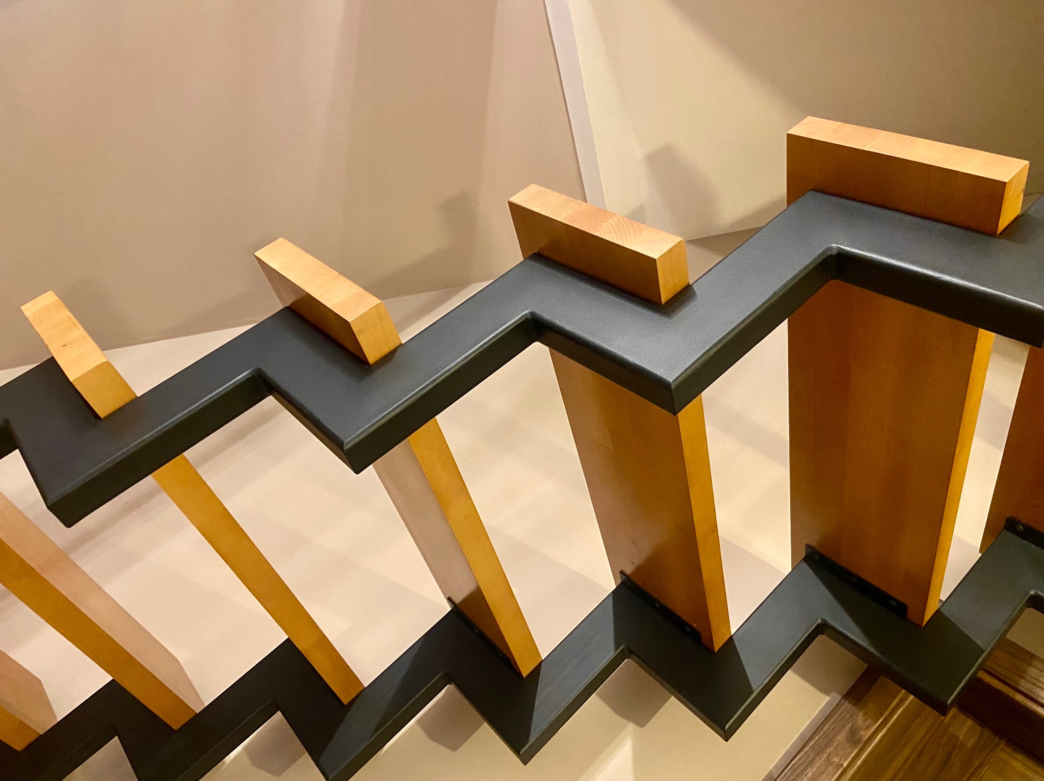 Nowoczesna balustrada schodowa z czarną metalową ramą i drewnianymi elementami wypełniającymi, widok z góry na schody z beżowymi ścianami w tle.