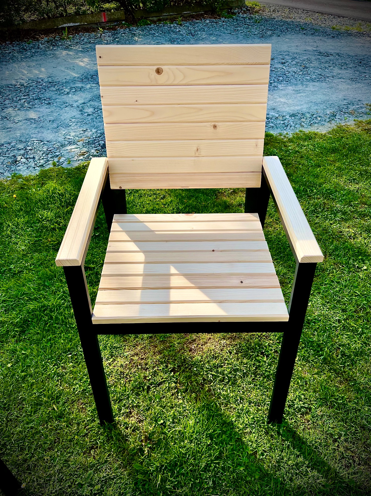 Drewniane krzesło z metalową ramą na trawie. Proste, minimalistyczne krzesło ogrodowe z jasnego drewna i czarnych nóg, ustawione na tle zielonego trawnika.