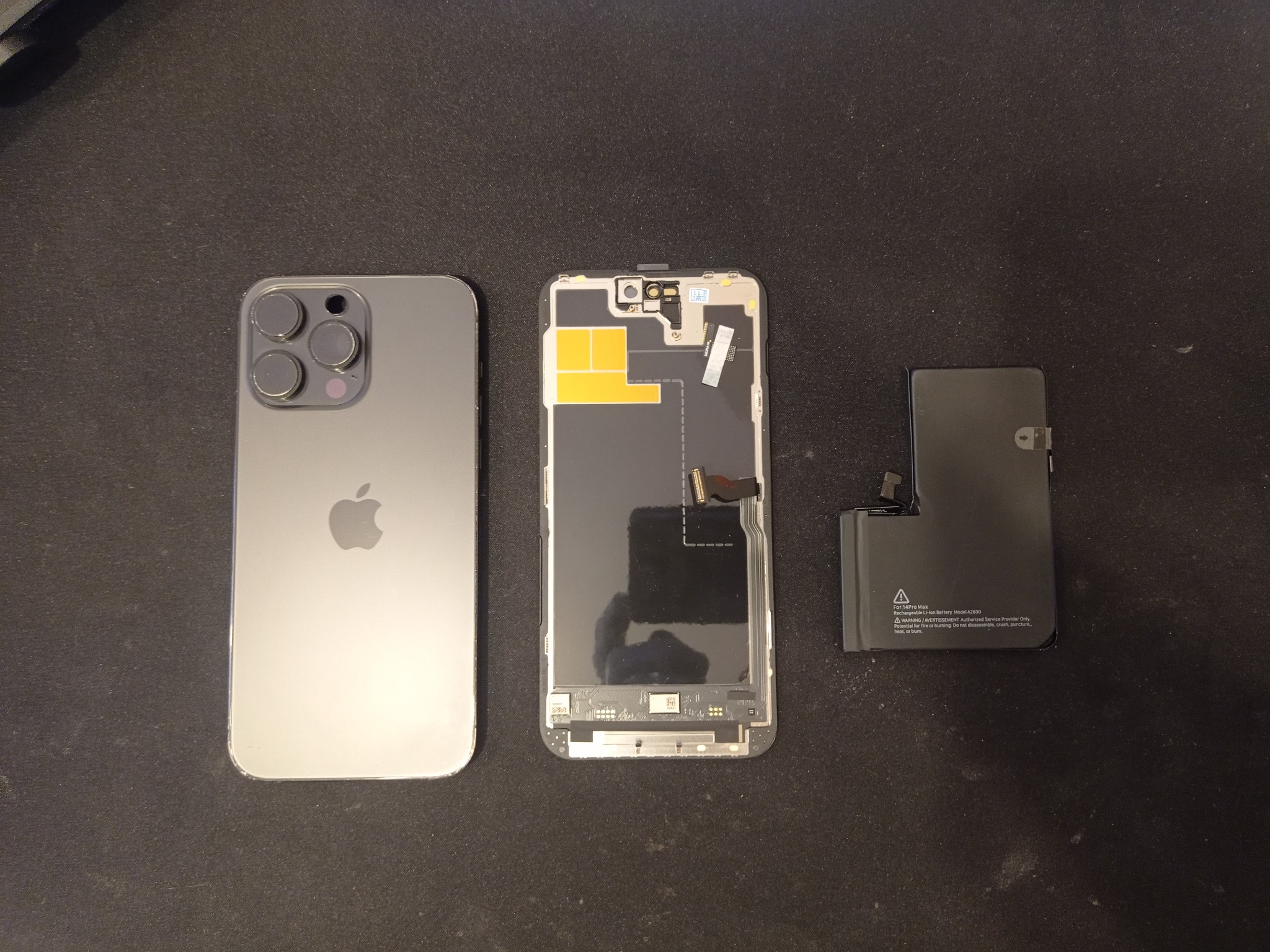 Rozłożony iPhone 14 Pro Max z widoczną baterią, obudową i elementami wewnętrznymi na czarnym tle.