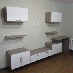 VIURPA SPÓŁKA Z OGRANICZONĄ ODPOWIEDZIALNOŚCIĄ - Nowoczesna zabudowa ściany z szafkami wiszącymi i dolnymi w kolorze białym i dębowym, z drewnianą podłogą i grzejnikiem żeliwnym pod oknem.