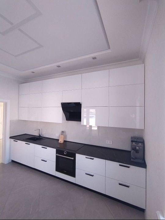 Biała kuchnia z górnymi szafkami pod sufit, czarnym blatem i czarnym okapem, widok z boku, minimalistyczny design.