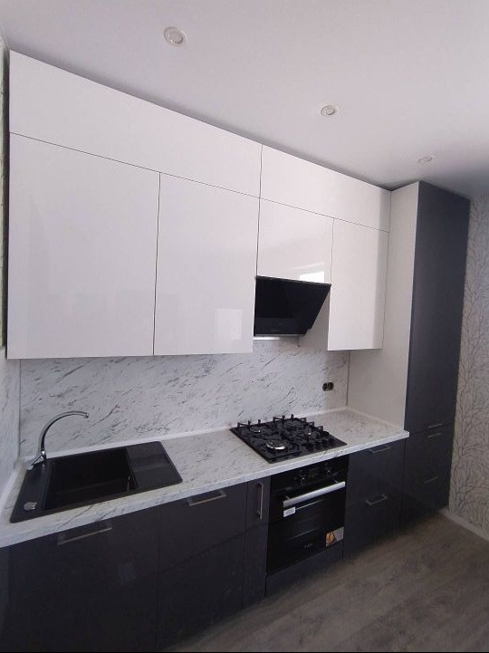 Nowoczesna kuchnia z białymi szafkami górnymi i grafitowymi dolnymi, marmurowy blat, czarna płyta gazowa i piekarnik, minimalistyczny okap.