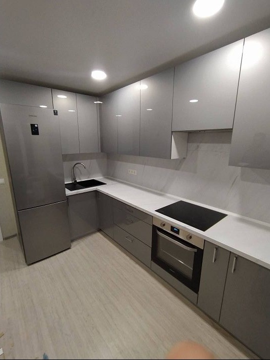 Nowoczesna kuchnia w szarych odcieniach z połyskującymi frontami, czarnym zlewem i płytą indukcyjną, jasny blat i podłoga imitująca drewno.