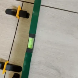 Układanie płytek podłogowych imitujących drewno, z użyciem poziomicy i klipsów do poziomowania, widoczne fugi.