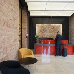 Sufity Napinane - Arkon System - Recepcja w nowoczesnym biurze z ceglanymi ścianami, podwieszanym sufitem z oświetleniem LED i elementami dekoracyjnymi, mężczyzna w garniturze przy ladzie.