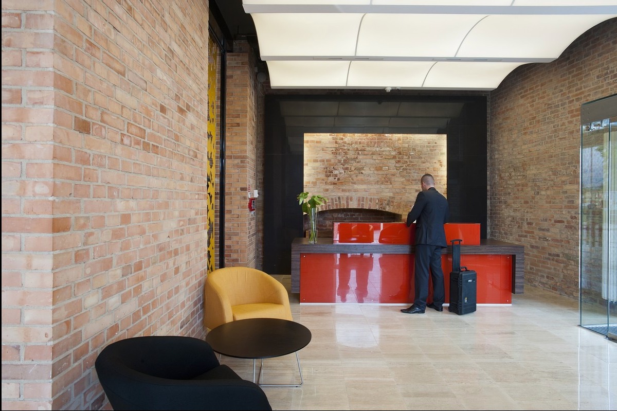 Recepcja w nowoczesnym biurze z ceglanymi ścianami, podwieszanym sufitem z oświetleniem LED i elementami dekoracyjnymi, mężczyzna w garniturze przy ladzie.