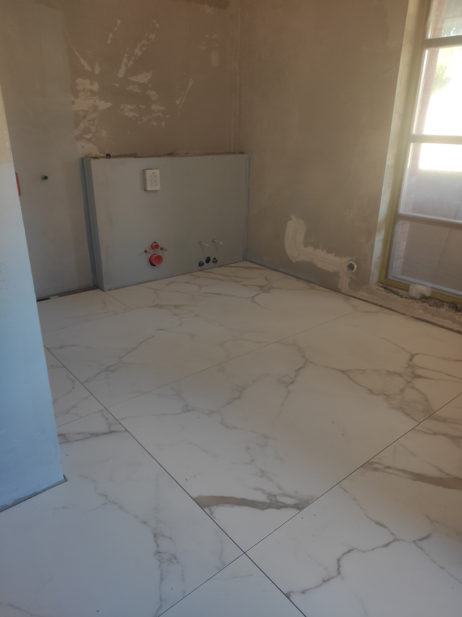 Łazienka w trakcie remontu, widoczne płytki podłogowe imitujące marmur, ściany przygotowane pod malowanie, instalacja podtynkowa WC ze stelażem i przyłączami wodnymi