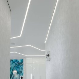 VIP GROUP TRADE SPÓŁKA Z OGRANICZONĄ ODPOWIEDZIALNOŚCIĄ - Białe, nowoczesne wnętrze z oświetleniem LED w suficie, widok na korytarz z dekoracyjną ścianą i szafą wnękową. Minimalistyczny design,  nowoczesne wykończenie.