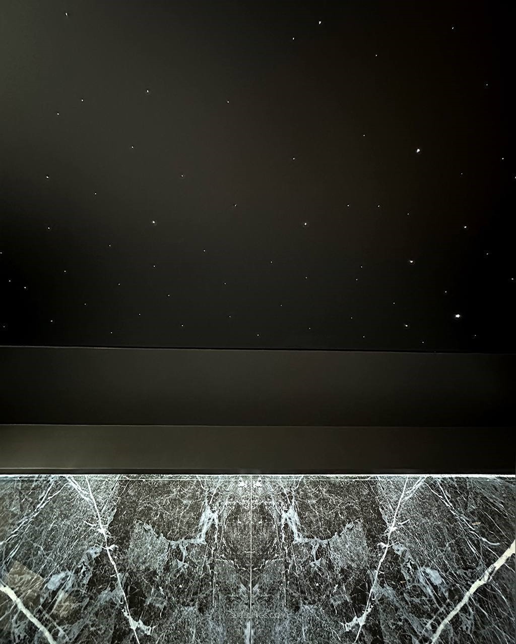 Ciemny sufit z punktowym oświetleniem imitującym gwiazdy, widoczny nad fragmentem ściany wykończonej ciemnym marmurem z białymi żyłami.
