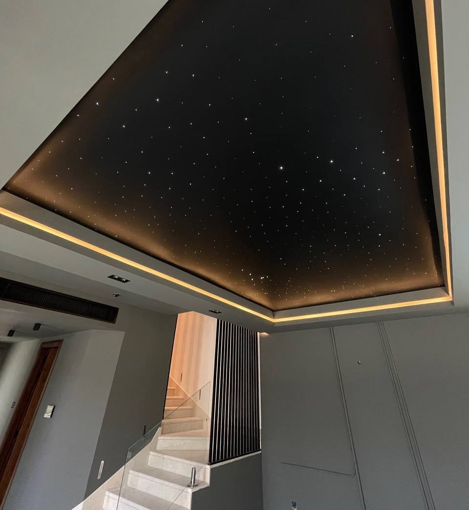 Czarny sufit z efektem rozgwieżdżonego nieba i subtelnym oświetleniem LED, widok z dołu, nowoczesne wnętrze z białymi schodami i szarymi ścianami.