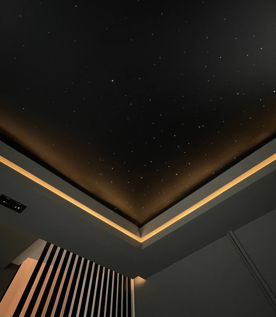 Sufit napinany imitujący nocne niebo z oświetleniem LED wzdłuż krawędzi sufitu i dekoracyjnym panelem ściennym z czarno-białymi paskami.