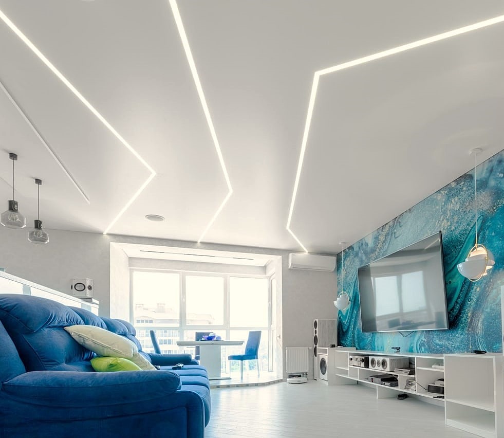 Nowoczesny salon z białym sufitem i geometrycznym oświetleniem LED. Niebieska sofa i akcentująca ściana dodają koloru. Minimalistyczny design wnętrza.
