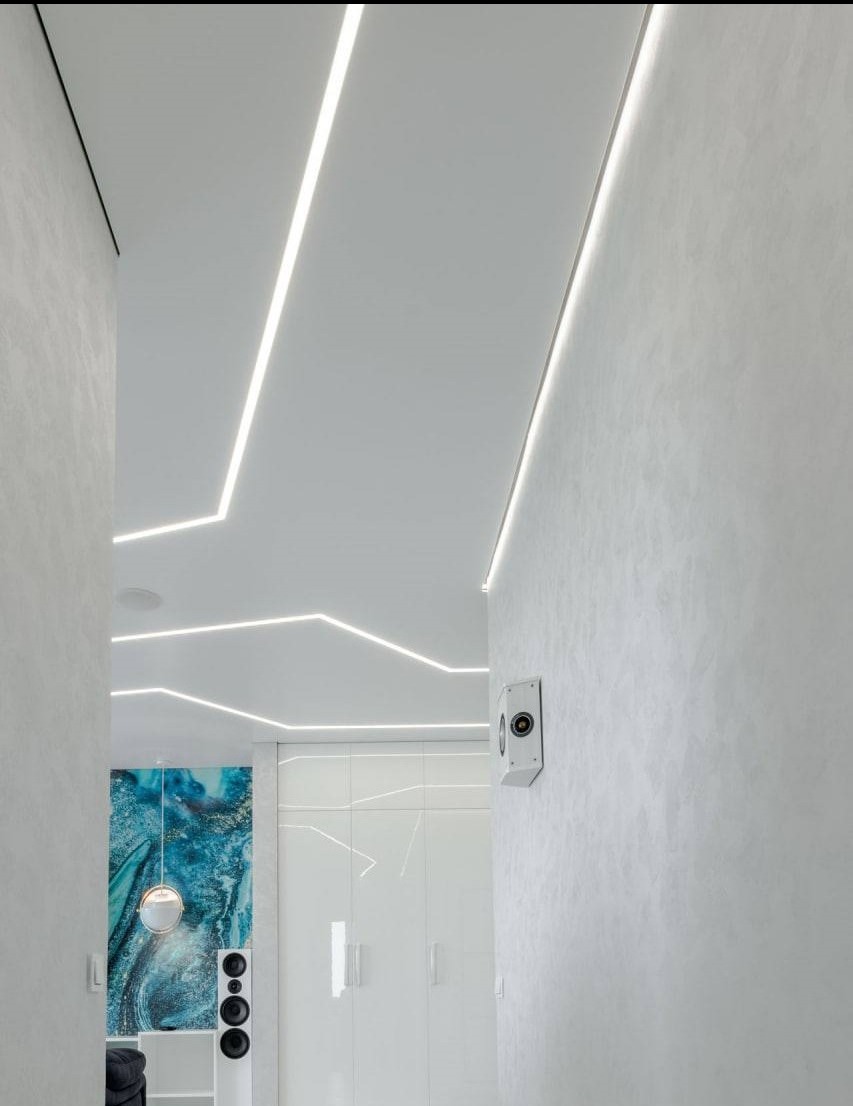 Białe, nowoczesne wnętrze z oświetleniem LED w suficie, widok na korytarz z dekoracyjną ścianą i szafą wnękową. Minimalistyczny design,  nowoczesne wykończenie.