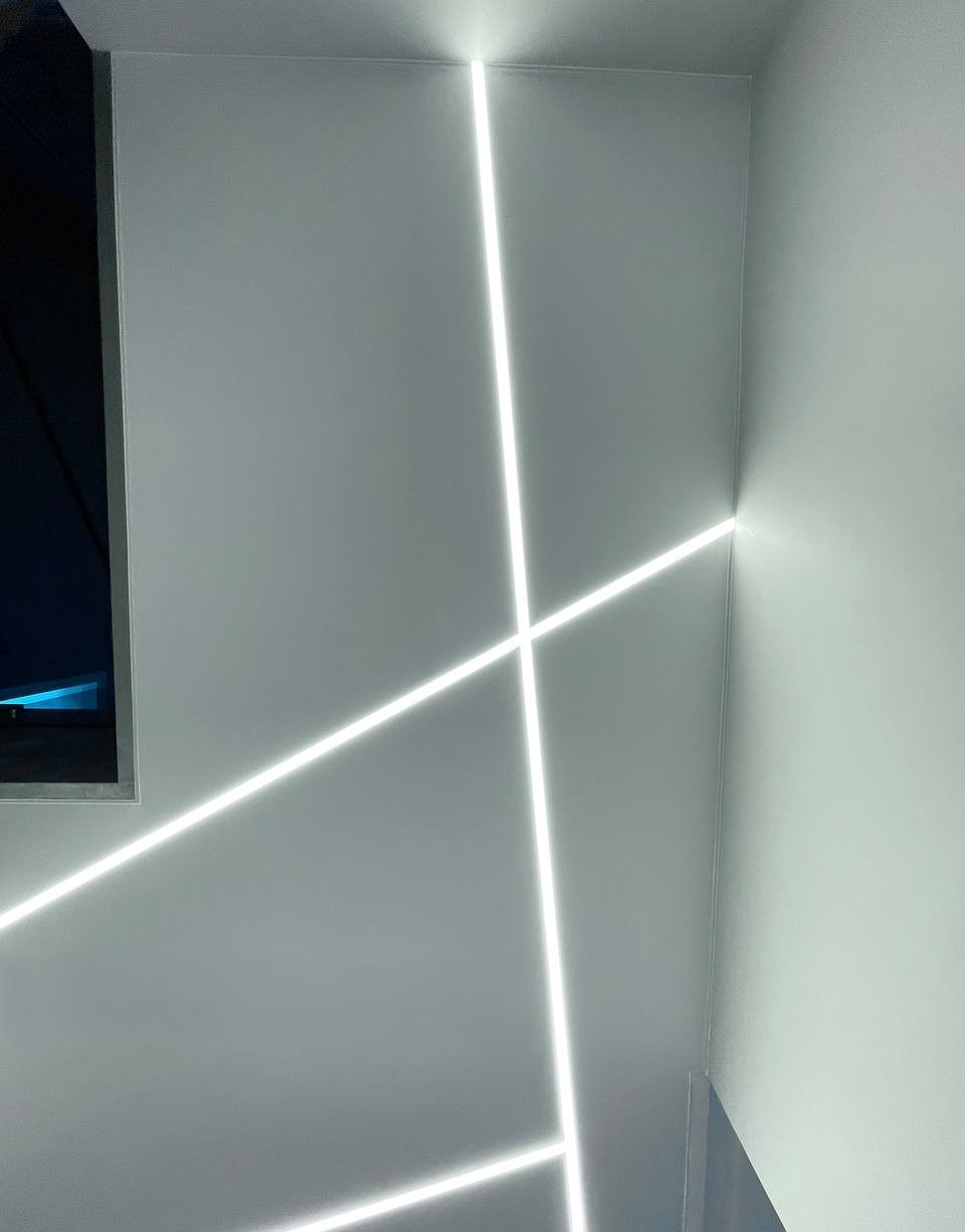 Minimalistyczne wnętrze z geometrycznym oświetleniem LED na ścianach, tworzącym nowoczesny i stylowy efekt wizualny w rogu pomieszczenia.