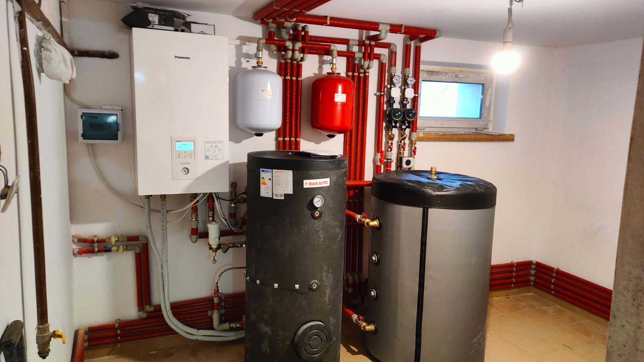 Zestaw urządzeń grzewczych w kotłowni: piec gazowy Panasonic, dwa zbiorniki buforowe Huch EnTEC, naczynia przeponowe i rozbudowana instalacja z rur w izolacji.