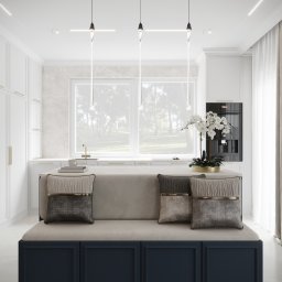 GES STUDIO Wykończenia wnętrz Sylwia i Wiktor Gęs - Elegancka kuchnia z wyspą, na której znajduje się siedzisko z dekoracyjnymi poduszkami, nowoczesne wiszące lampy z transparentnymi elementami, w tle marmurowa ściana i okno z widokiem na zieleń.