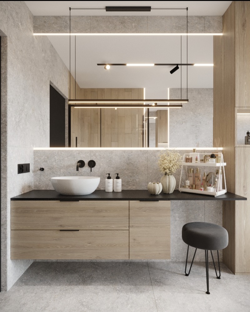 Nowoczesna łazienka z kamienną ścianą, okrągłą umywalką nablatową, drewnianą szafką z czarnym blatem, podświetlanym lustrem i szarym stołkiem na cienkich nogach.