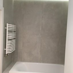 Odynets Aleksandr - Minimalistyczna łazienka z wanną, grzejnikiem drabinkowym i szarymi płytkami. Podświetlenie LED nadaje nowoczesny charakter. Ujęcie z perspektywy wejścia.