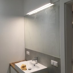 Odynets Aleksandr - Nowoczesna łazienka po remoncie w Siemianowicach Śląskich. Biała umywalka z drewnianym blatem, duże lustro z oświetleniem LED i szare płytki.