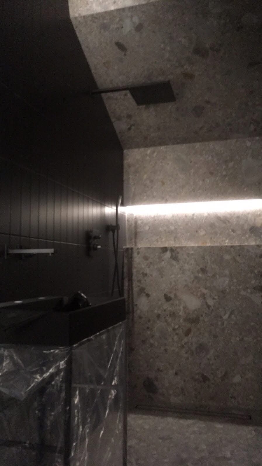 Nowoczesna łazienka w Siemianowicach Śląskich z czarnymi płytkami i kamienną mozaiką, oświetlona listwą LED. Minimalistyczny design z deszczownicą.