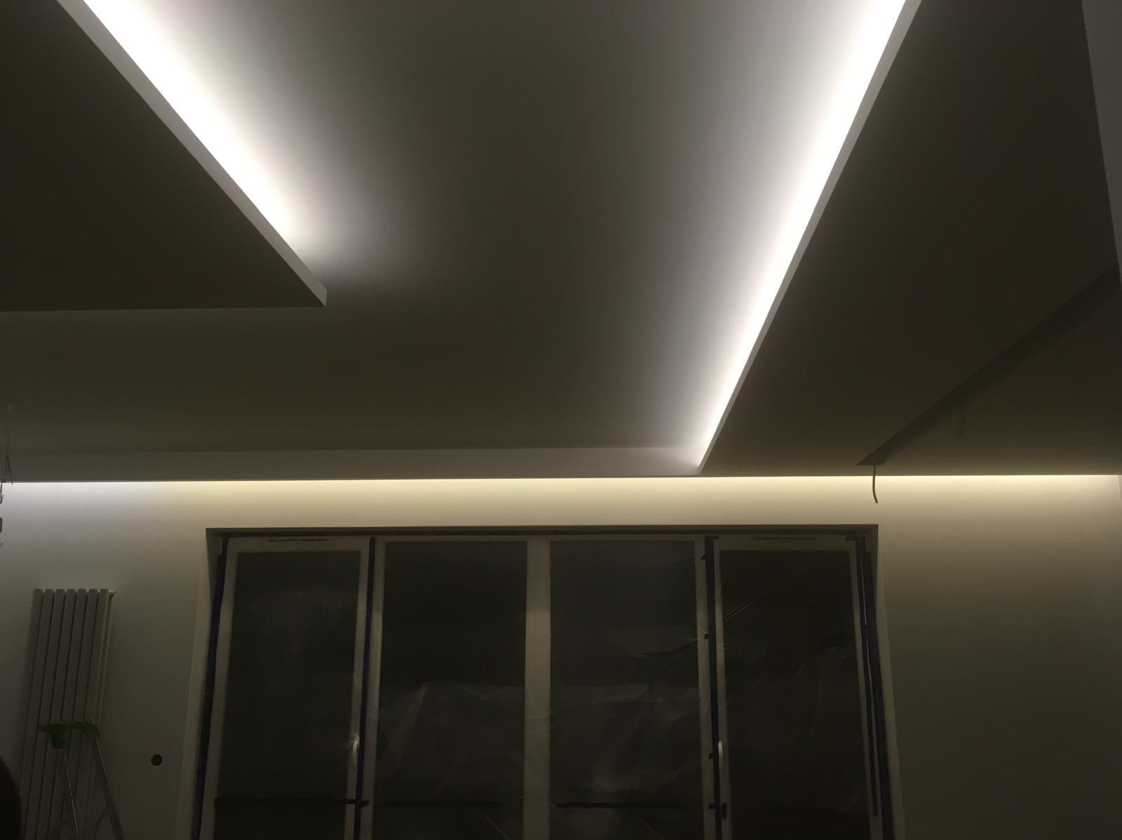 Nowoczesne oświetlenie sufitowe LED w wykończonym wnętrzu. Geometryczne wzory świetlne podkreślają minimalistyczny design. Widoczny fragment okna i grzejnika.