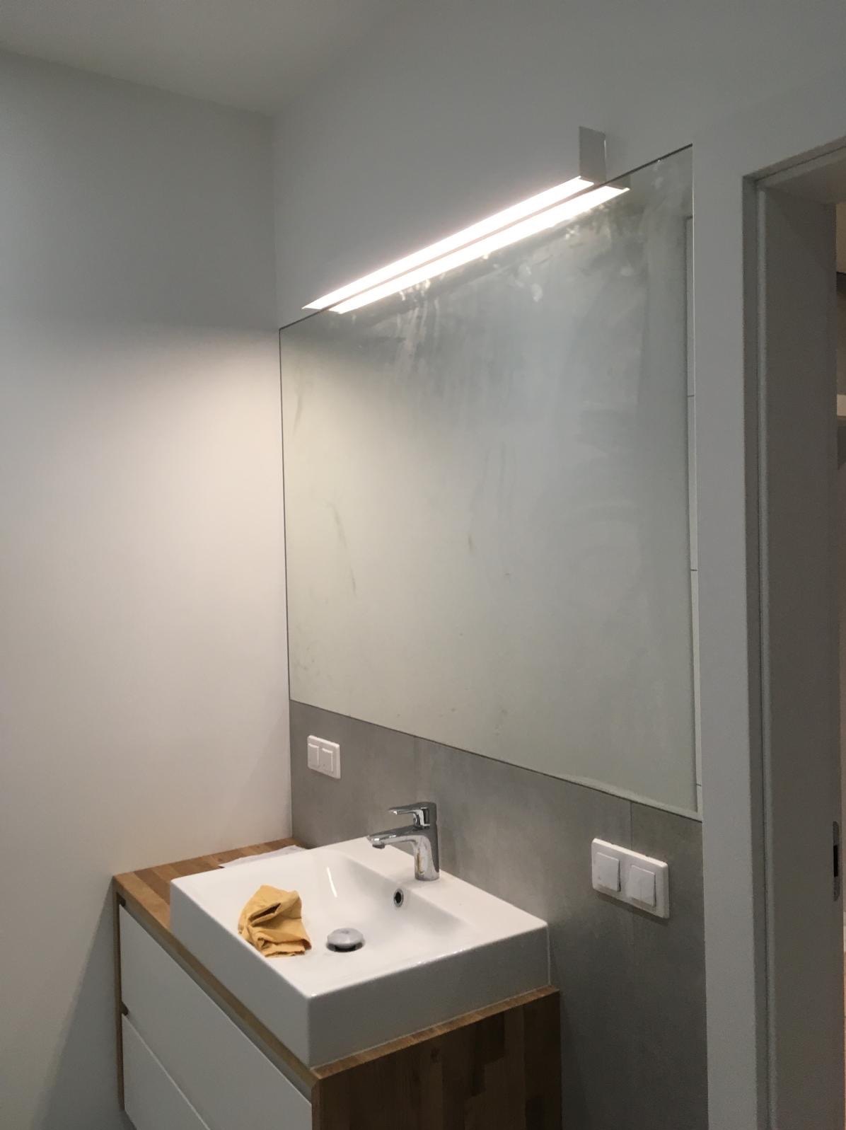 Nowoczesna łazienka po remoncie w Siemianowicach Śląskich. Biała umywalka z drewnianym blatem, duże lustro z oświetleniem LED i szare płytki.