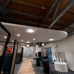 Elektronauts Sp. z o.o. - Nowoczesne biuro z drewnianą podłogą, metalową konstrukcją sufitu i oświetleniem punktowym, widok na przestrzeń otwartą z biurkami i krzesłami.