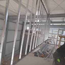 Kris-bau - Metalowa konstrukcja ścian działowych w trakcie montażu w przestronnym, jasnym pomieszczeniu. Widoczne narzędzia i drabina.