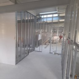 Kris-bau - Wnętrze w trakcie prac wykończeniowych z widocznymi metalowymi profilami konstrukcyjnymi ścian działowych i fragmentem płyty gipsowo-kartonowej.