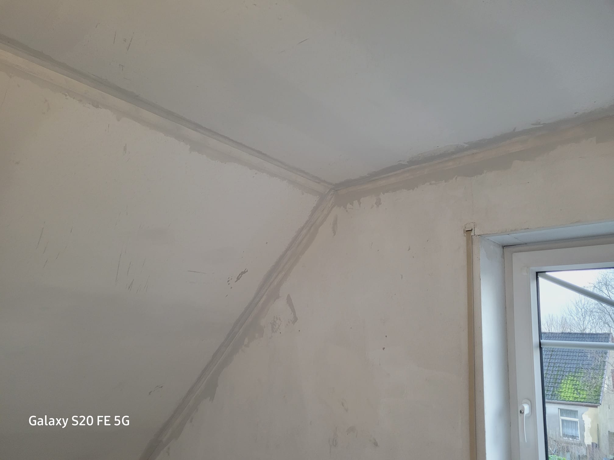 Ściana i sufit po nałożeniu gładzi, widoczne niedoskonałości i ślady po szpachlowaniu, przygotowane do malowania, okno w tle