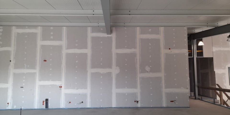 Ściana z płyt gipsowo-kartonowych w trakcie szpachlowania, widoczne łączenia płyt, przygotowana pod malowanie. Widoczne instalacje elektryczne.