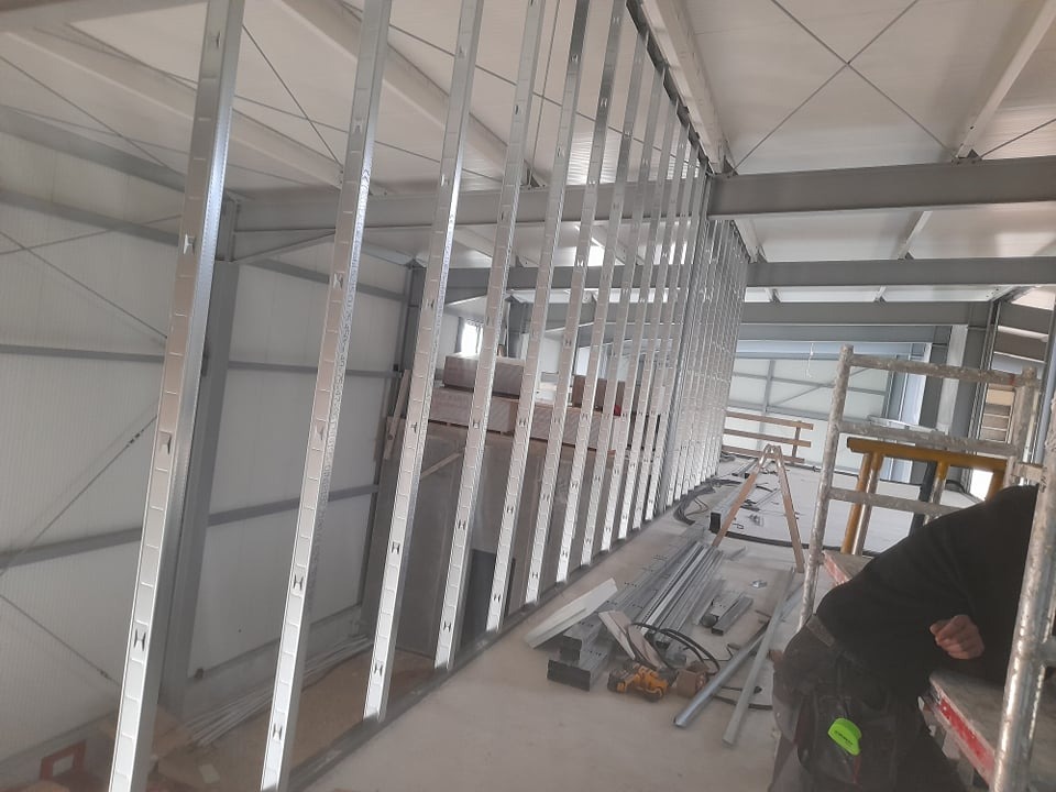 Metalowa konstrukcja ścian działowych w trakcie montażu w przestronnym, jasnym pomieszczeniu. Widoczne narzędzia i drabina.