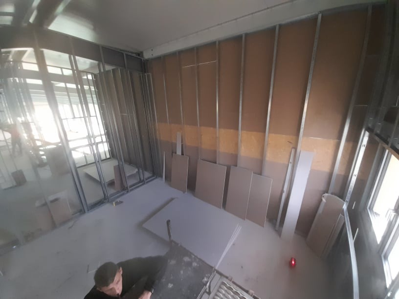 Wnętrze w trakcie zabudowy ścian działowych z płyt kartonowo-gipsowych na metalowym stelażu, widok z góry na elementy konstrukcyjne i przygotowane płyty.