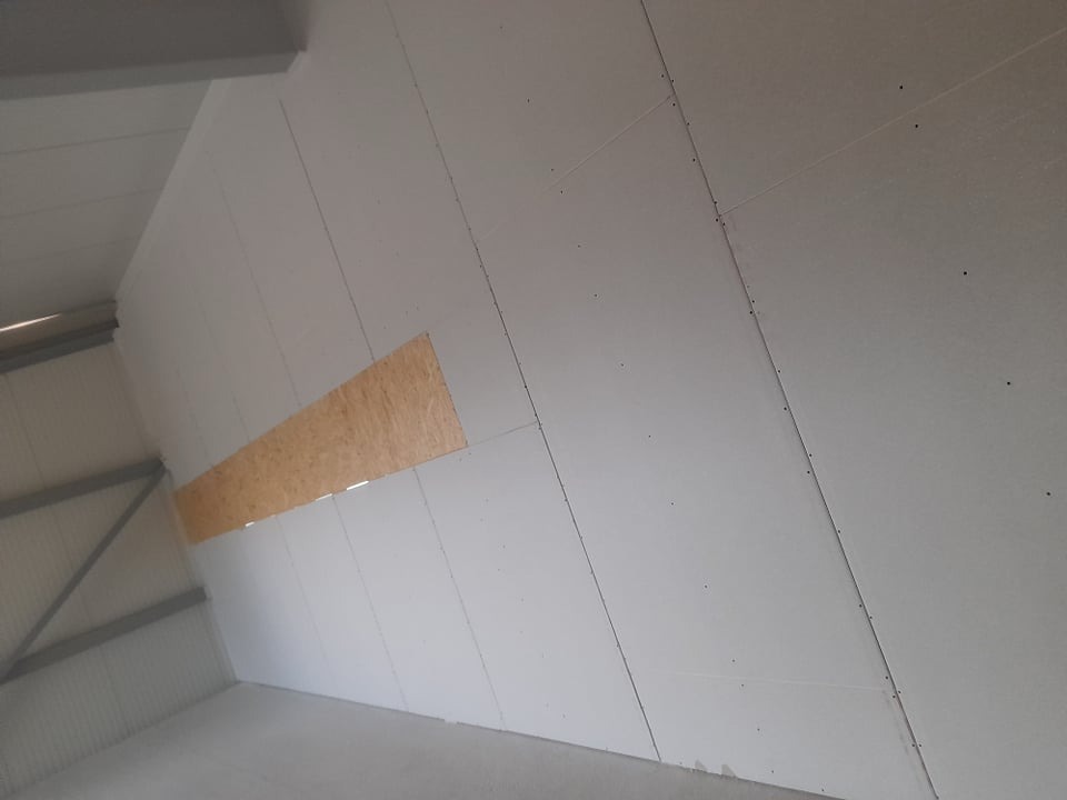 Płyty gipsowe na poddaszu w Skrwilnie, zamontowane pod skosem, z widocznym fragmentem drewnianej konstrukcji. Prace wykończeniowe wewnątrz budynku.