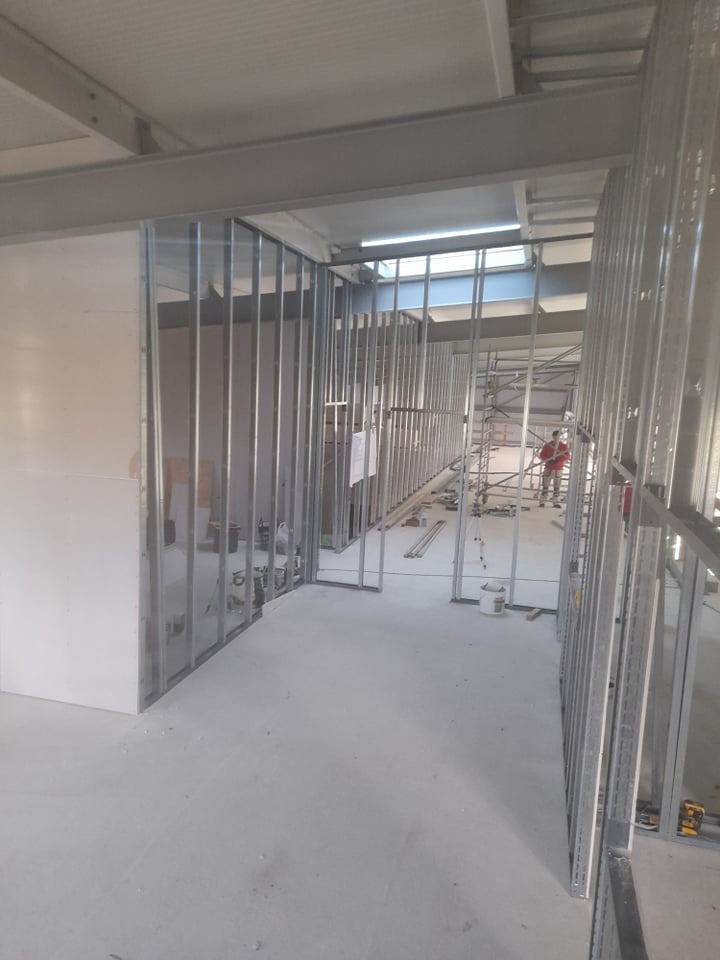 Wnętrze w trakcie prac wykończeniowych z widocznymi metalowymi profilami konstrukcyjnymi ścian działowych i fragmentem płyty gipsowo-kartonowej.