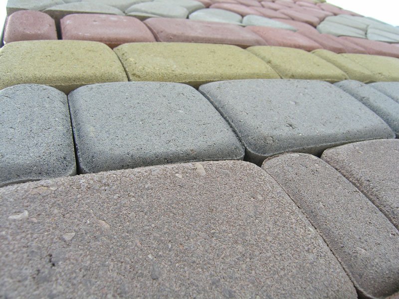 Ułożona, wielokolorowa kostka brukowa z bliska, widoczne różne odcienie szarości, beżu, żółci i różu, z zaokrąglonymi krawędziami, ukazana pod kątem.