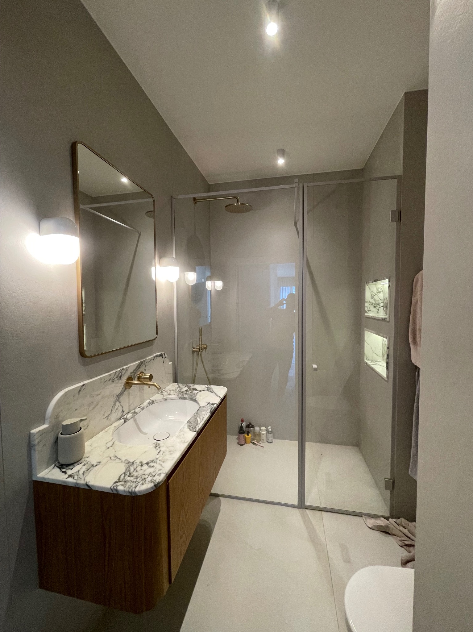 Nowoczesna łazienka z kabiną prysznicową typu walk-in, umywalką nablatową z marmurowym blatem i złotą armaturą oraz wnękami w ścianie wykończonymi marmurem.