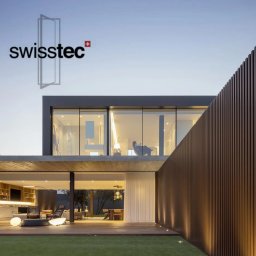 Swisstec Okna i Drzwi - Nowoczesny dom z dużymi przeszkleniami i drewnianą fasadą, logo firmy widoczne na górze.