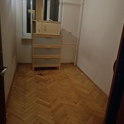 Clean Protection Katarzyna Hejno - Pusty pokój z parkietem w jodełkę i drewnianą komodą z nadstawką przy oknie.