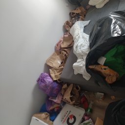 Clean Protection Katarzyna Hejno - Zabrudzone mieszkanie z workami śmieci, kartonami po pizzy, torbami i innymi odpadami na podłodze i kanapie. Widok z góry na bałagan.
