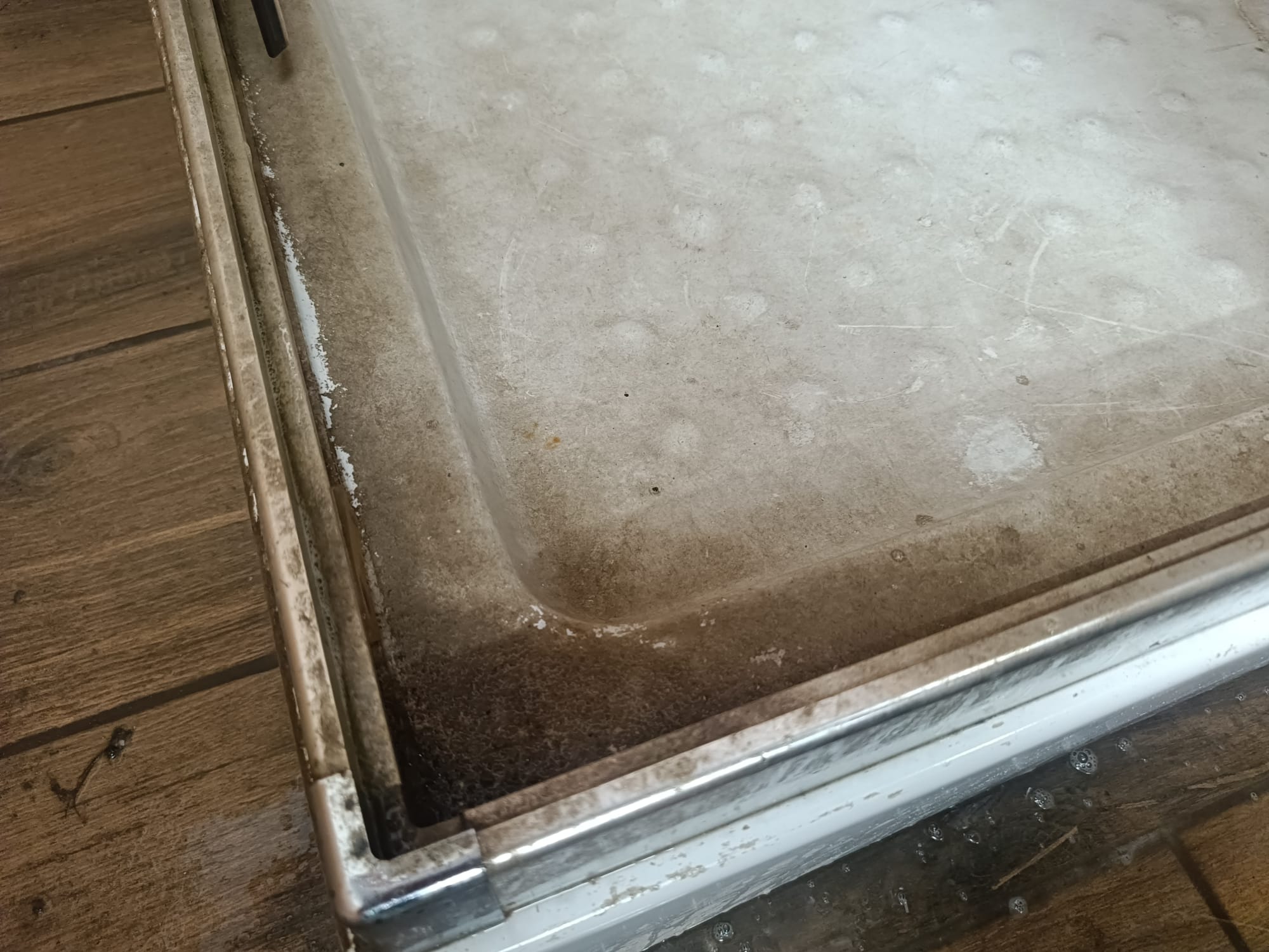 Silnie zabrudzona, biała brodzik kabiny prysznicowej z widocznymi zaciekami i osadami, częściowo wypełniona wodą z mydlinami, ujęcie z góry.