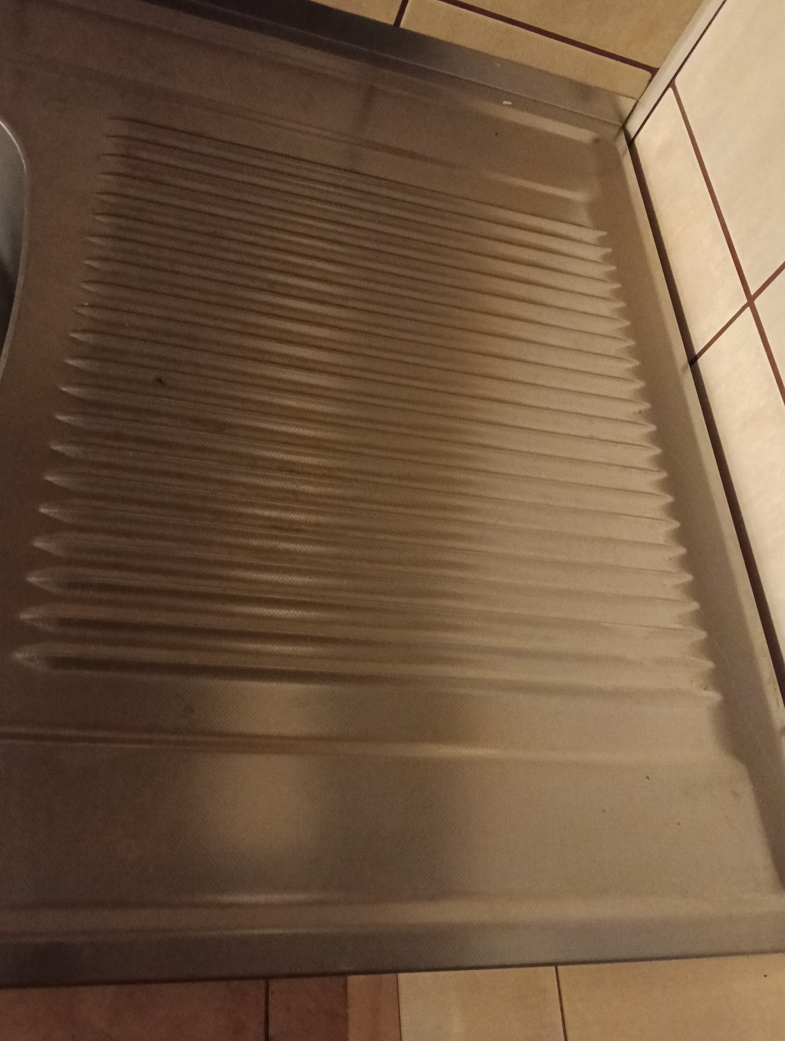 Wnętrze łazienki z widoczną umytą, metalową wanną z pralką w tle, po zakończonym sprzątaniu. Widoczne płytki na ścianie i podłodze.