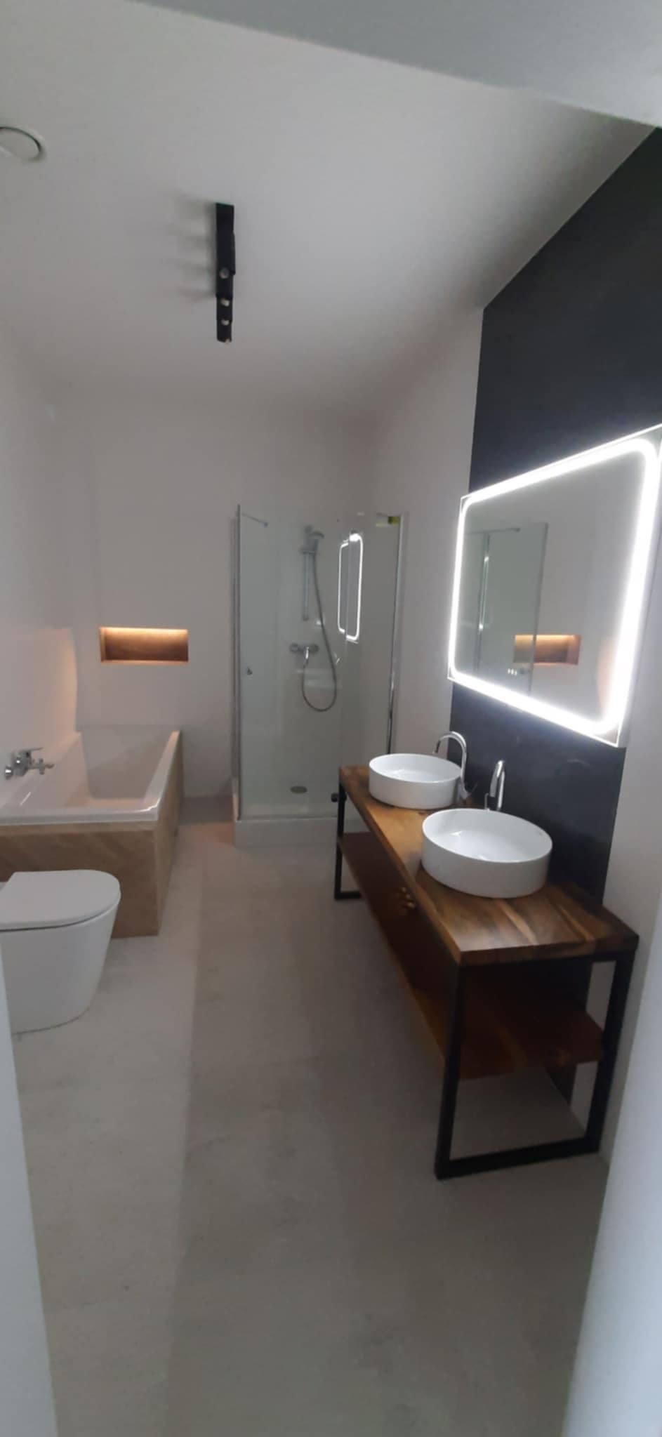 Nowoczesna łazienka z drewnianą szafką pod umywalki, podświetlanym lustrem i kabiną prysznicową. Minimalistyczny design z akcentami drewna i czerni.