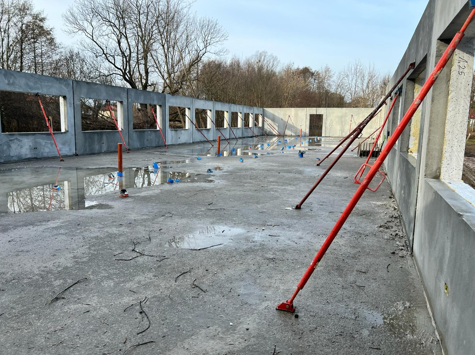 Surowy stan budynku w Warszawie z żelbetu, widoczne podpory i mokra posadzka po wylaniu betonu, przygotowywane otwory okienne.