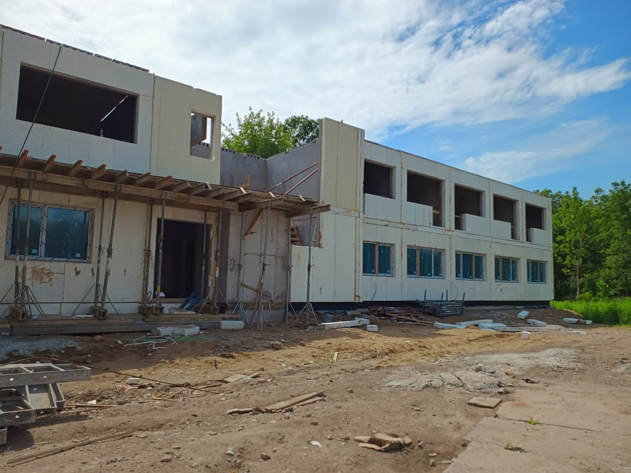 Budowa dwukondygnacyjnego budynku modułowego z betonu komórkowego, widoczne rusztowania i niezagospodarowany teren budowy.