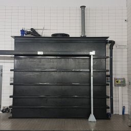 INSTAL-ART S.C. T. KLOC, S. DUDEK. - Czarna, segmentowa oczyszczalnia ścieków w pomieszczeniu z białymi kafelkami, widoczna drabina i panel sterowania.