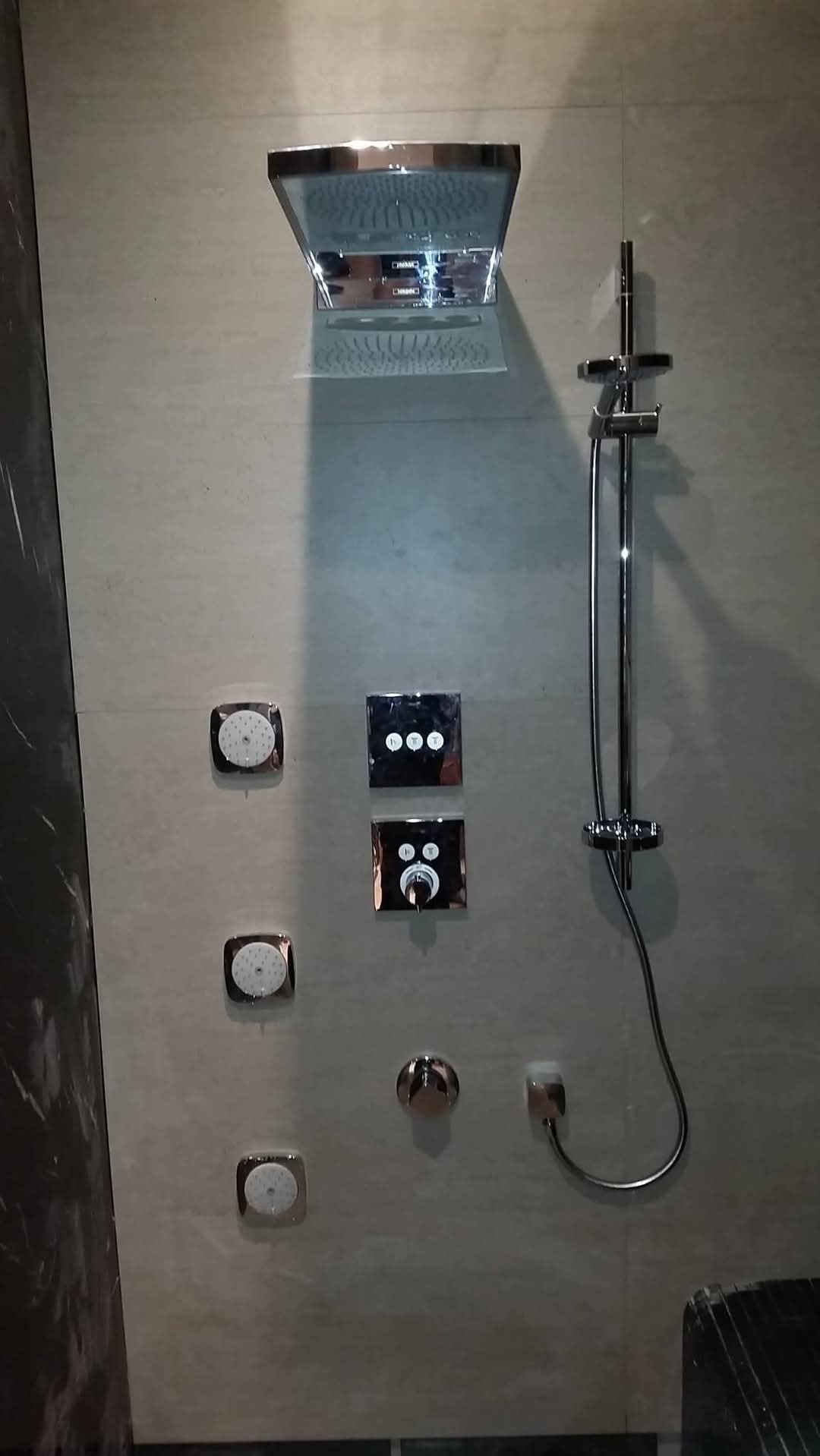 Nowoczesny panel prysznicowy z deszczownicą, baterią termostatyczną i kilkoma dyszami natryskowymi, zamontowany na jasnej, marmurkowej ścianie w łazience.