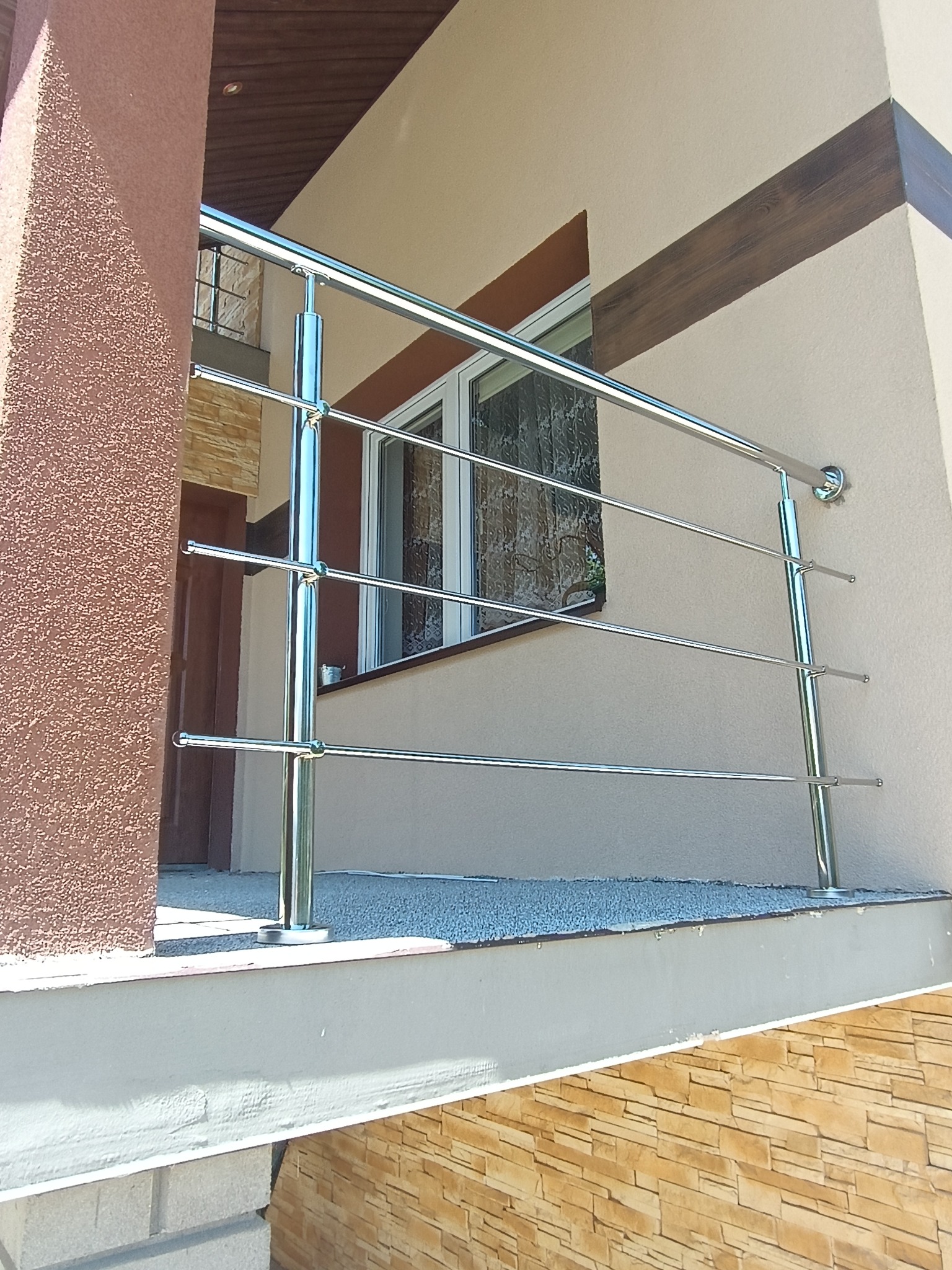 Elegancka, czteroprzęsłowa balustrada ze stali nierdzewnej, zamontowana na balkonie. Widoczne detale mocowania do ściany i wykończenie słupków.